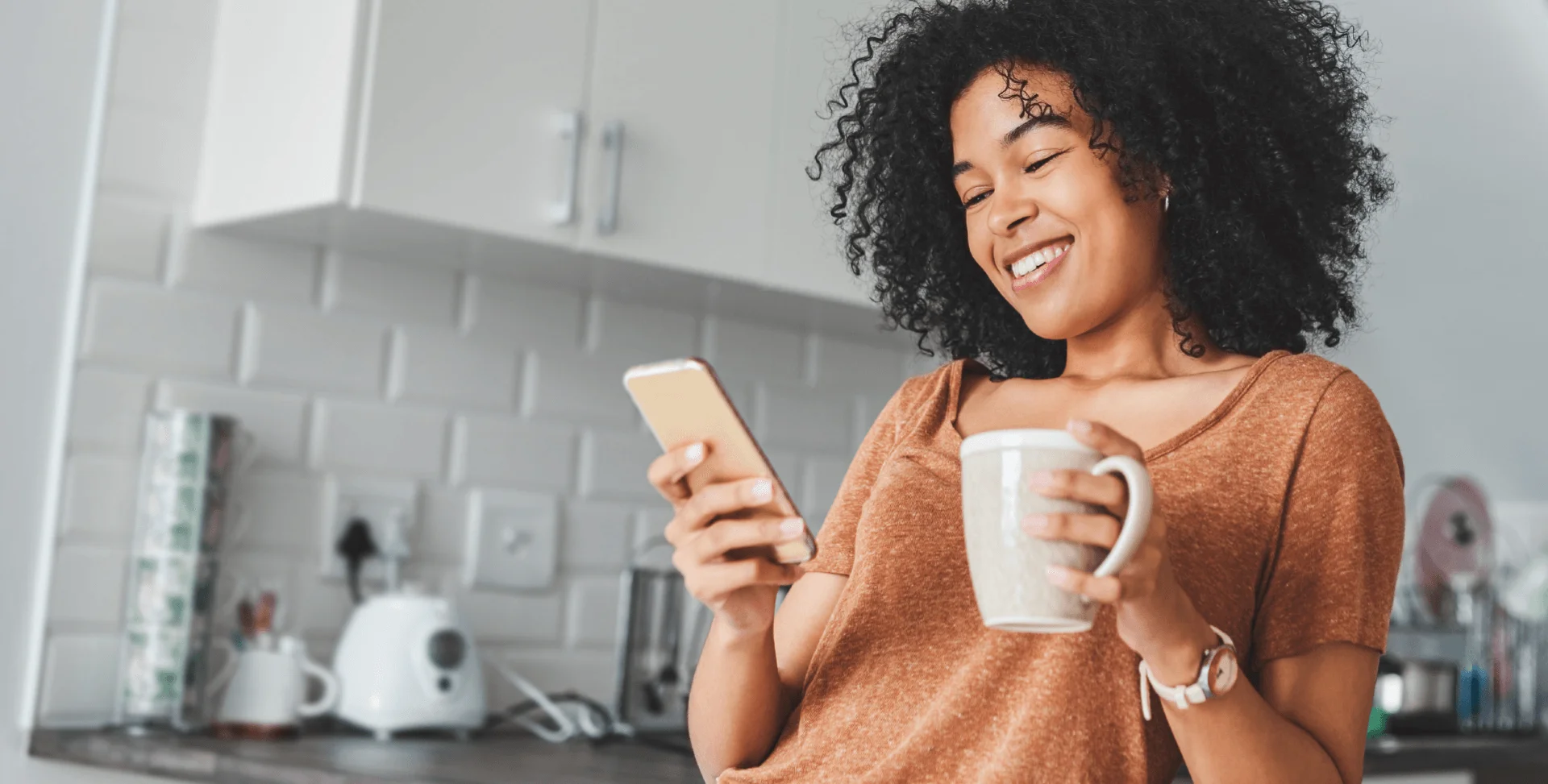 A smiling woman holds a cup of coffee and reads her phone