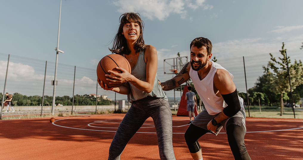 A man and woman outside playing basketball