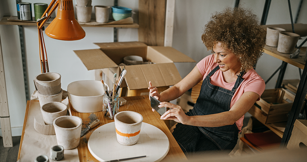 A woman in a pottery studio taking a photo of her work