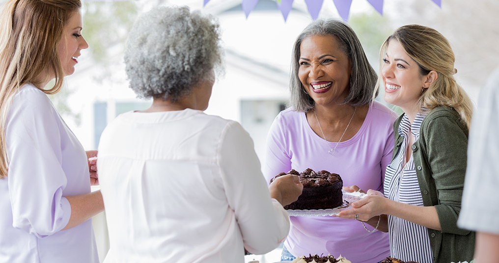 Four women chatting together and sharing a cake.