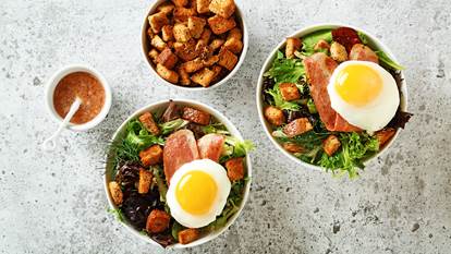 Bistro turkey bacon salad with a sunny side egg on top and a bowl of croutons on the side.