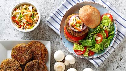 Mushroom squash burgers on a plate with a bun, salad, tomatoes and whole mushrooms on the side.