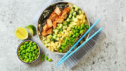 Salmon poke style salad in a bowl with blue chopsticks and edamame and lime on the side