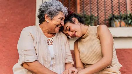 Two women holding hands with one resting her head on the other’s shoulder.