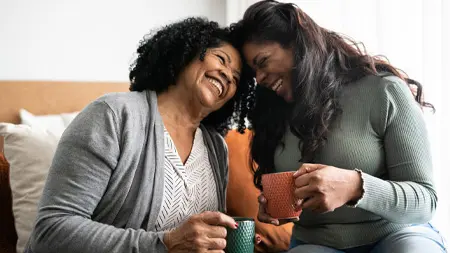Two women having an intimate laugh while holding mugs.