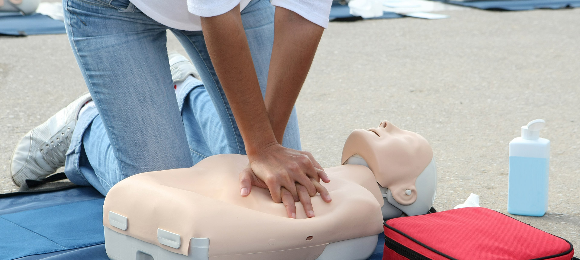 A woman performs chest compressions on a mannequin during an outside CPR training session