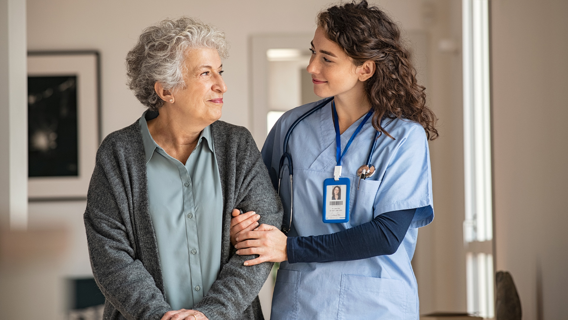 A young nurse holds an elderly woman’s arm to support her.