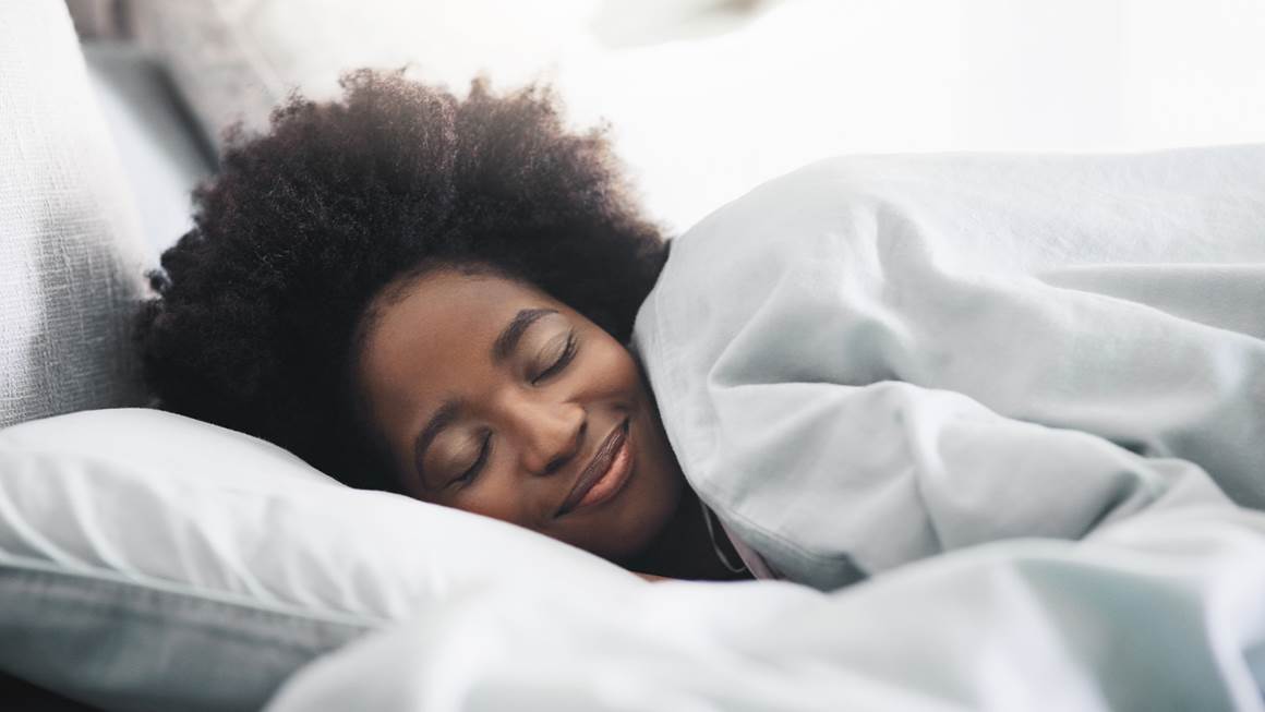 A smiling woman sleeps on a bed.
