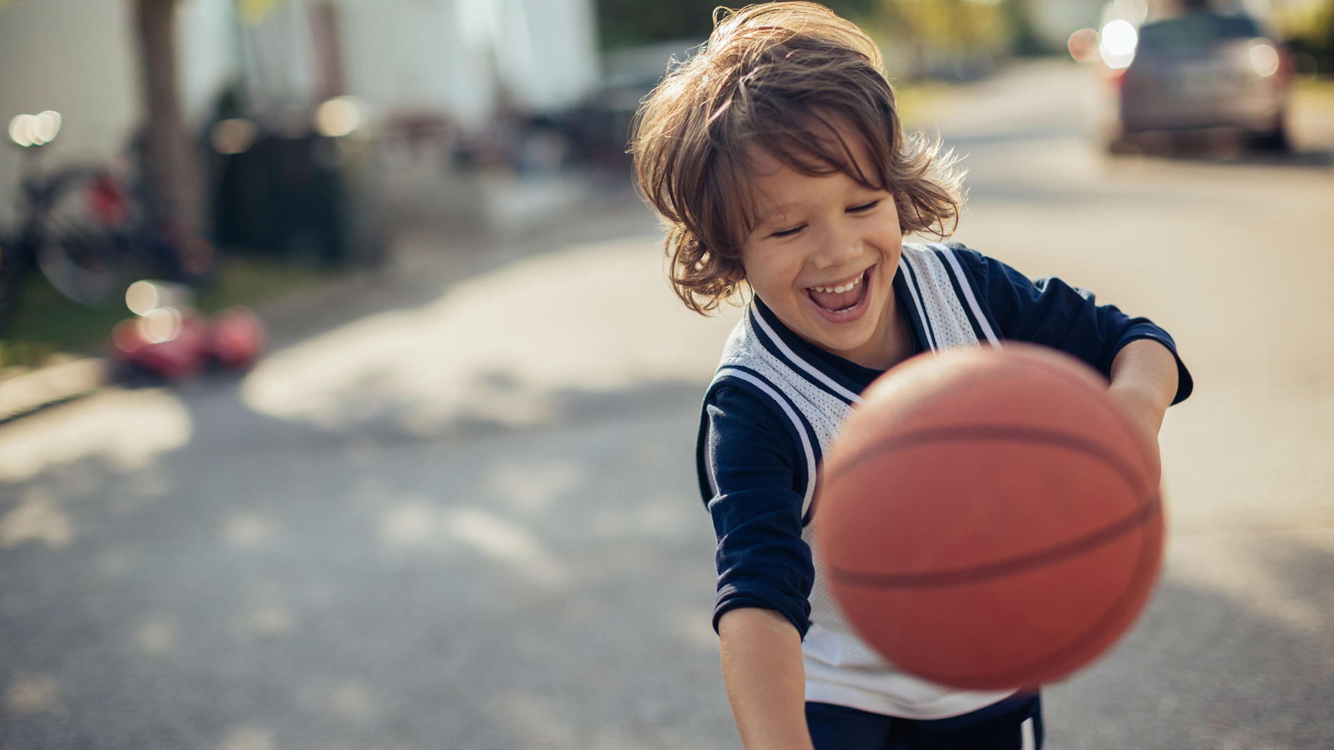 Little boy is smiling while  playing with a basketball on a suburban street