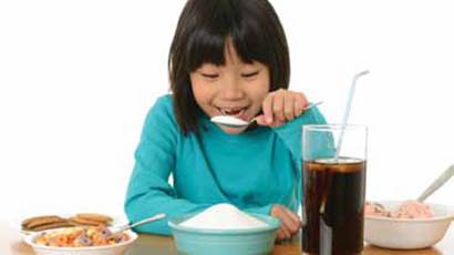 A smiling girl pretends to eat a large spoonful of sugar from a blue bowl