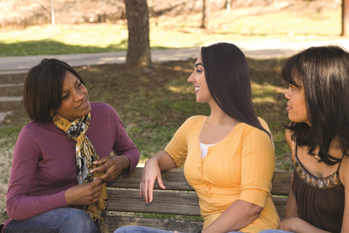 Three women sitting on a bench engaged in conversation.