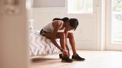 Young woman in her bedroom tying her running shoe