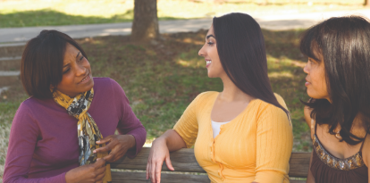 Three women sitting on a bench engaged in conversation.