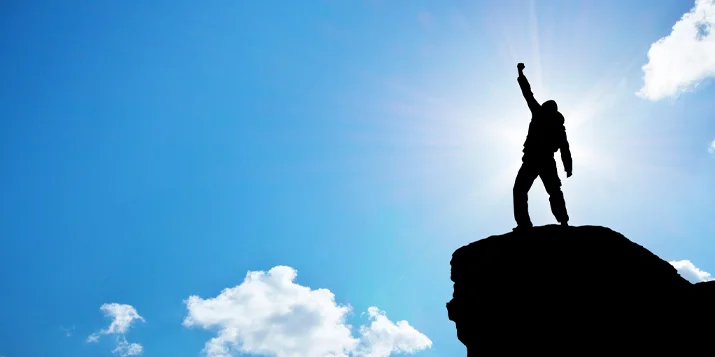 A silhouette of a person lifting an arm in victory while facing the clouds.