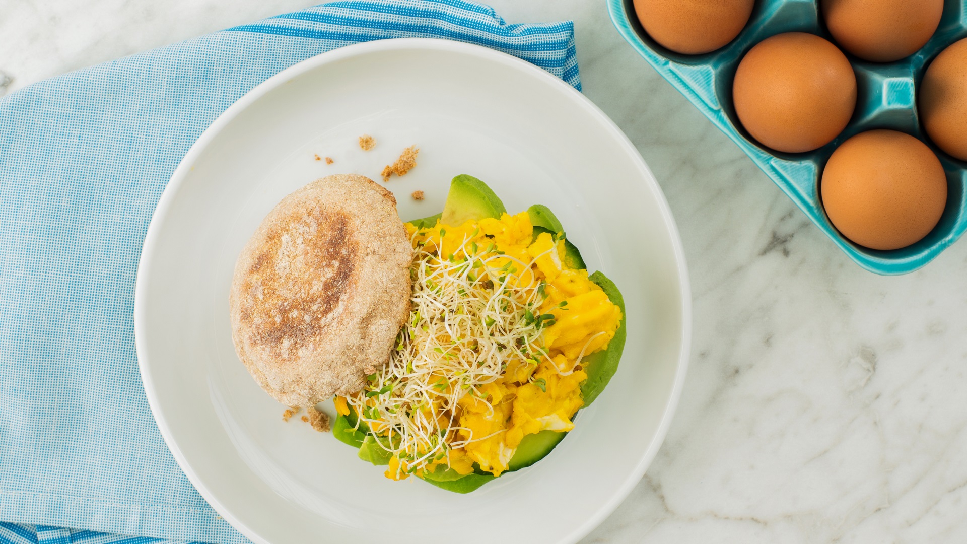 Avocado and egg breakfast sandwich on a white plate on top of a marble countertop