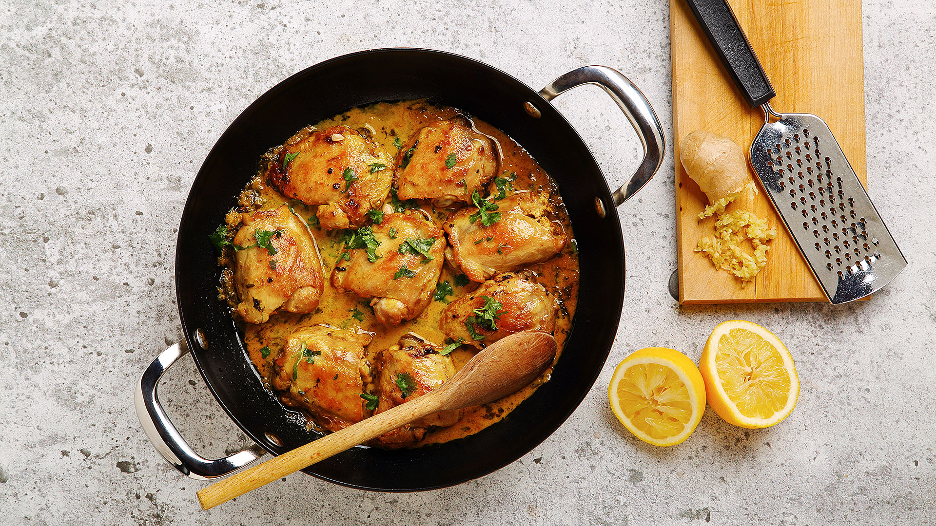 Curried lemon ginger chicken in a large skillet with grated ginger and cut lemon on the side.