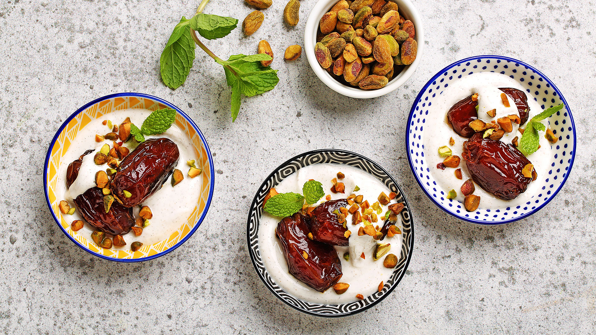 Three bowls of pan fired dates with cardamom yogurt with mint leaves and pistachios.