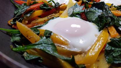 Sauteed bell peppers and spinach with fried eggs in a skillet