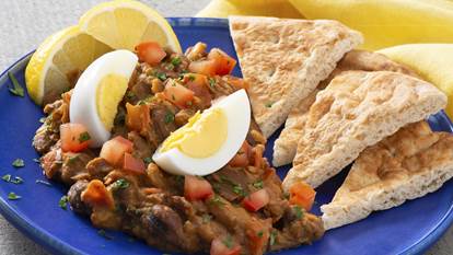 Egyptian fava bean foule with slices of pita bread and lemon wedges on a bright blue plate.