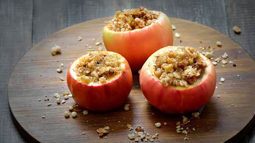 Three baked red apples on a wooden board with granola filling. 