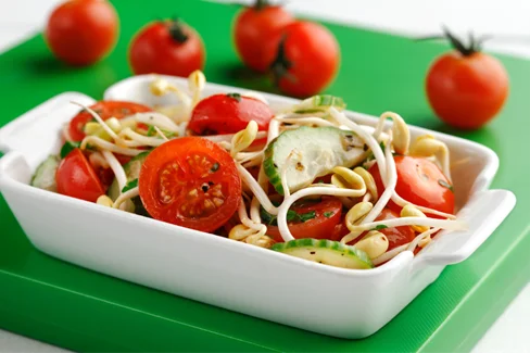 Bean sprouts and tomatoes in a white dish on a green board