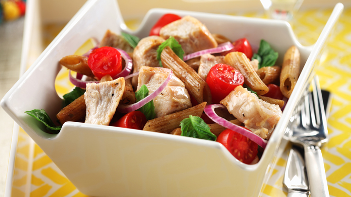 Bistro chicken pasta salad in a square white bowl with a fork on a yellow tablecloth