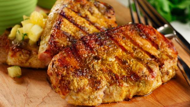 Close up of grilled pork chops on cutting board with sliced pineapple 