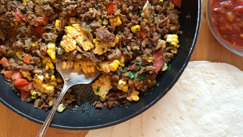 Filling for mushroom beef tacos in a black bowl with tortillas and salsa on the side.