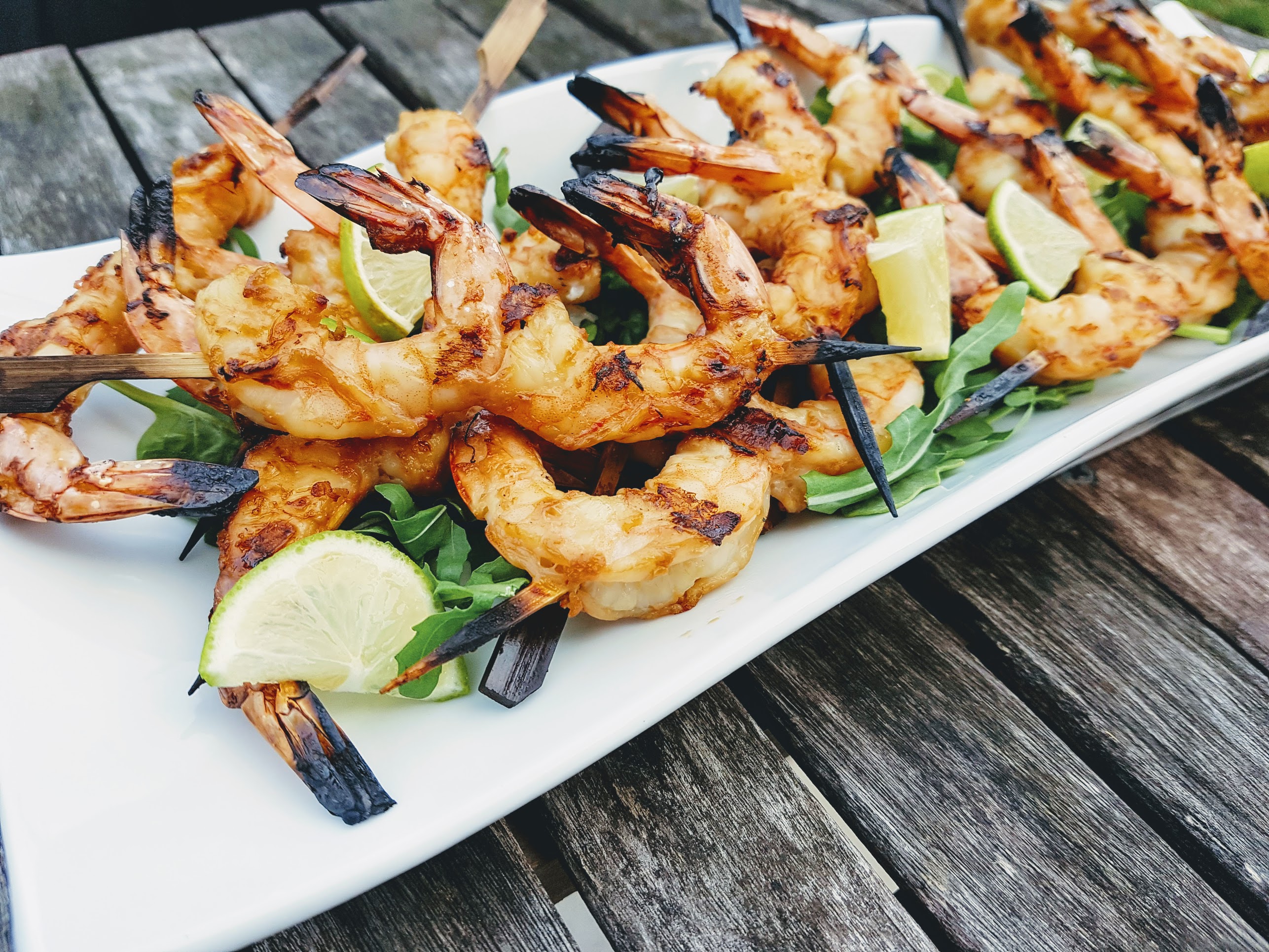 Pile of grilled shrimp skewers on a bed of arugula