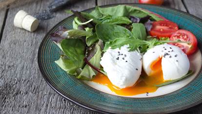 Poached eggs on plate with green salad and tomatoes