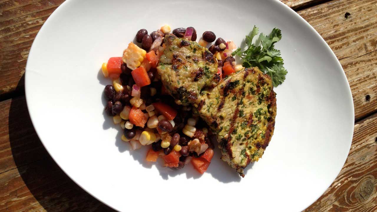 Pork with black bean salad on a large white plate on a wooden table