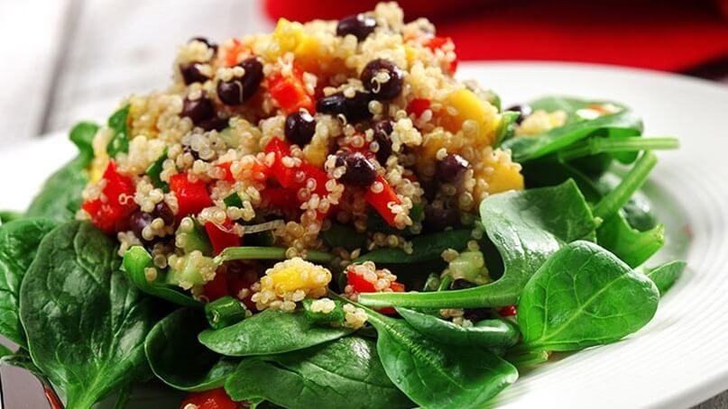 Cooked quinoa, chopped red peppers, mango and black beans on a bed of spinach