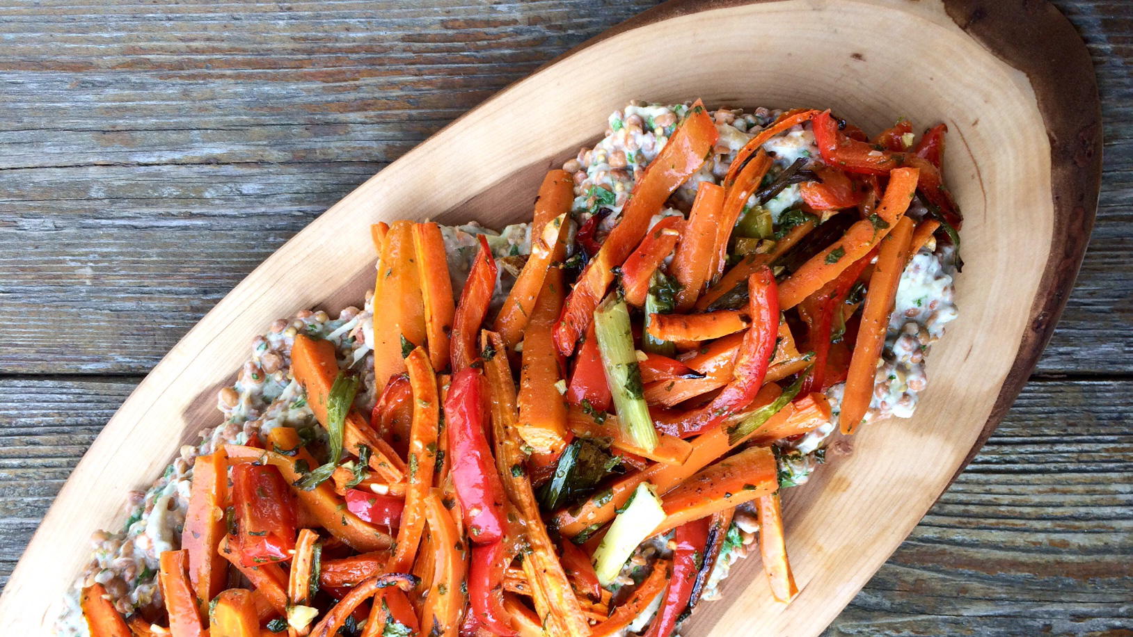 Shredded roasted carrot and eggplant overtop lentils served in wooden platter