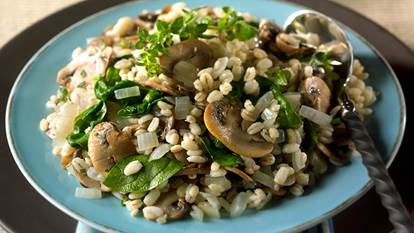 Spinach and mushroom barley pilaf served on a blue plate with a spoon on the side