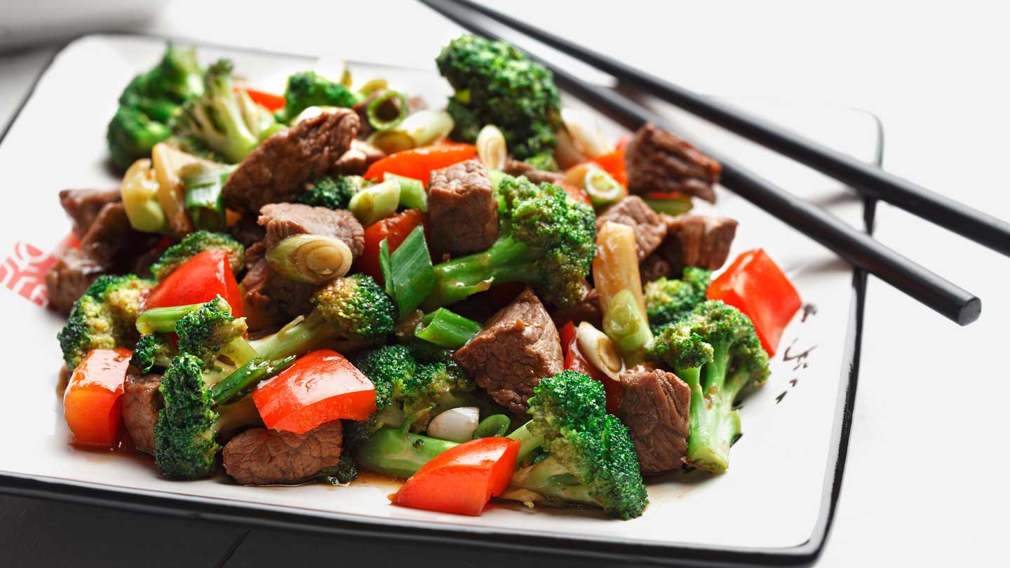 Stir fried broccoli red peppers and beef on a white plate with chopsticks
