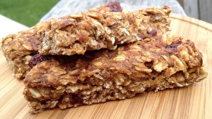 Three cranberry granola bars on a wooden cutting board