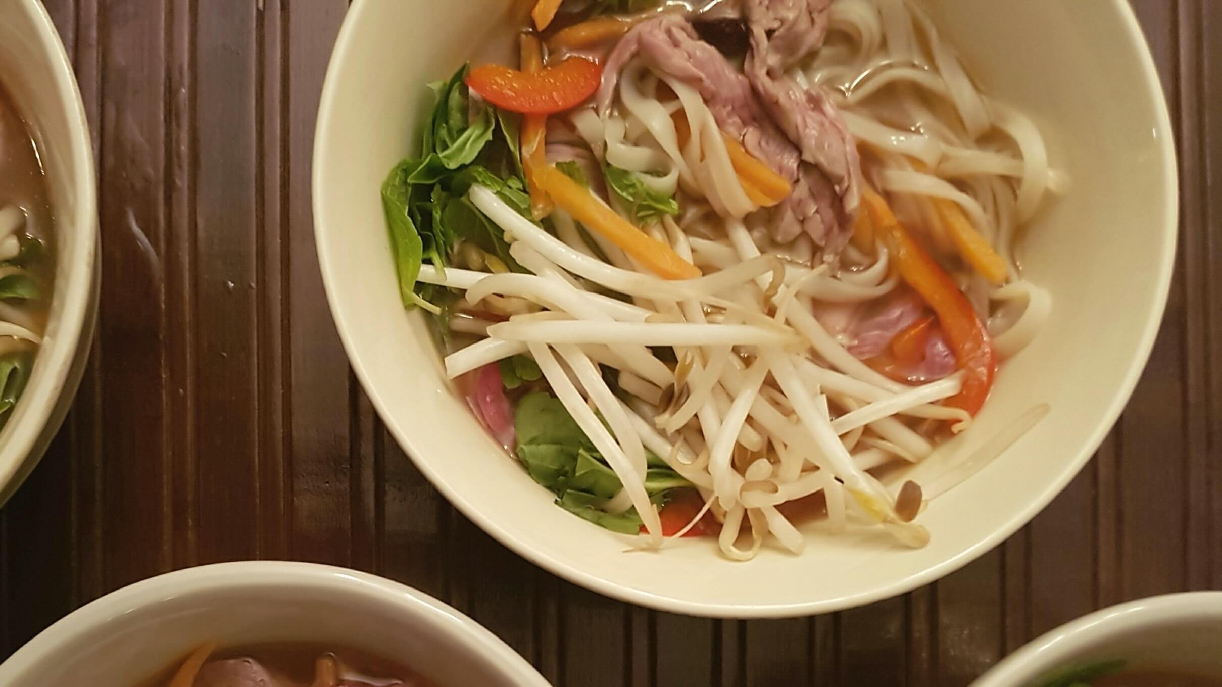 Bowl of noodles, beans spouts, beef, red peppersm spinach and broth