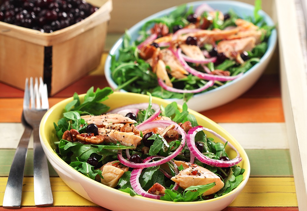 Bowls of arugula topped with cooked salmon, onion and blueberries