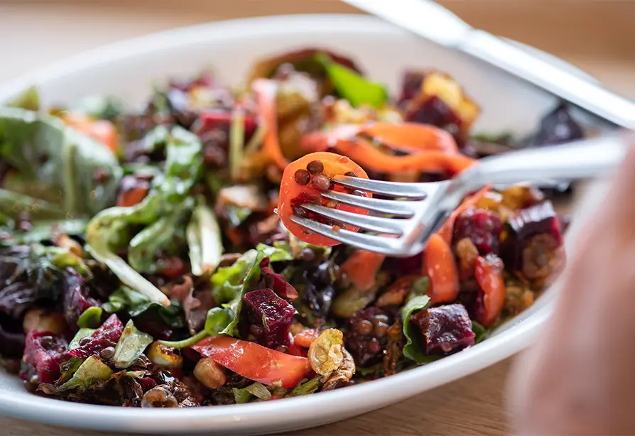 A fork picking from a bowl of roasted beet, brussels sprouts and other vegetables.