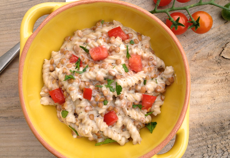 A yellow bowl of lentil macaroni and cheese, topped with chopped tomatoes and parsley