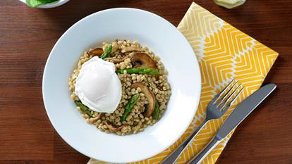 Poached egg with mushroom barley pilaf in a white serving bowl on top of a yellow patterned napkin. 