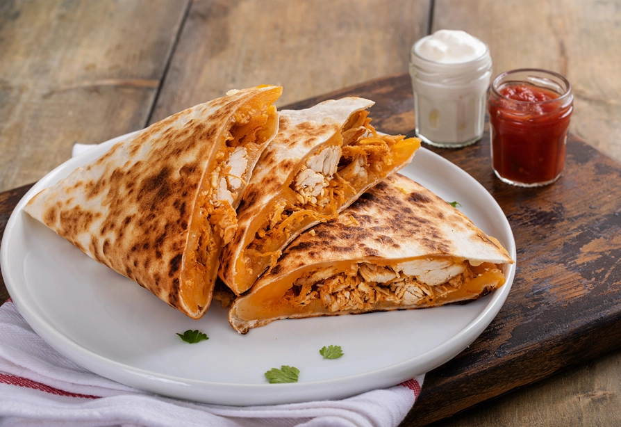 Chicken and sweet potato quesadilla on a white plate with salsa and sour cream in the background.