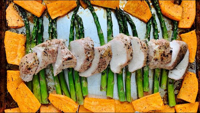 Pork tenderloin on a baking sheet with sweet potatoes and asparagus