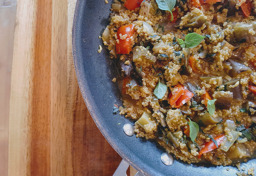 A skillet of quinoa, red bell peppers, eggplant, topped with fresh herbs
