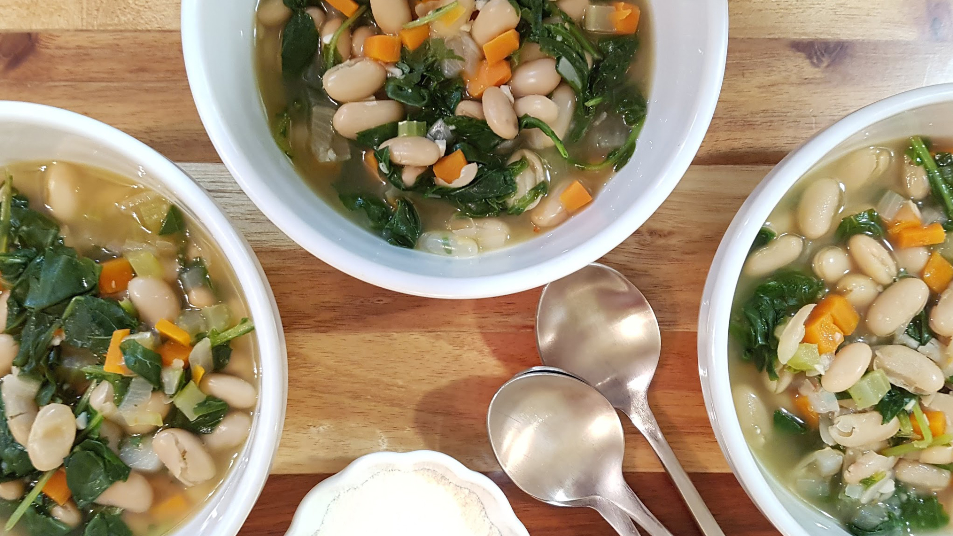 Three bowls of white bean and vegetable soup on a wooden table.