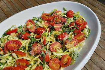 Plate of spiralled zucchini noodles, sliced cherry tomatoes and basil