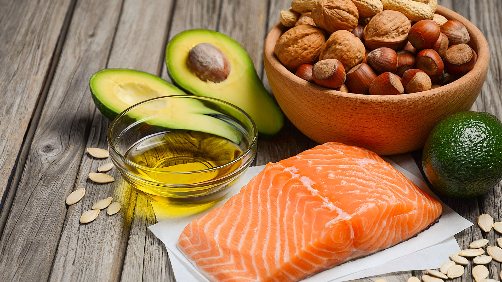 Selection of healthy fat sources: salmon, nuts, seeds, avocados and olive oil.