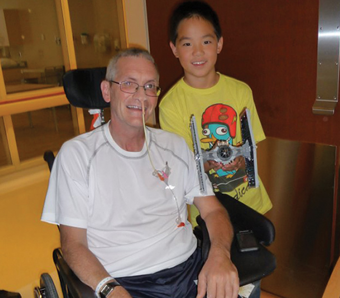 Young child standing next to his dad who is sitting on a wheelchair, dealing with stroke recovery
