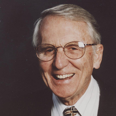 A man wearing a suit with his face towards camera. He is mid-laugh.