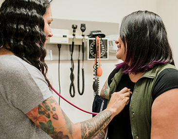 A woman uses a stethoscope to listen to another woman’s heart in an Indigenous health clinic.